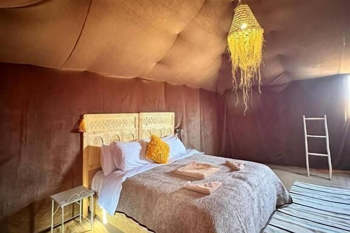 A cozy, dimly lit room with a bed, a small table, and a hanging light fixture.