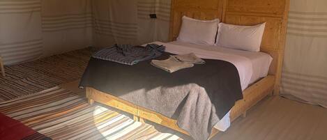 A cozy, striped-patterned tent with a wooden bed, a woven light fixture, and a patterned rug.