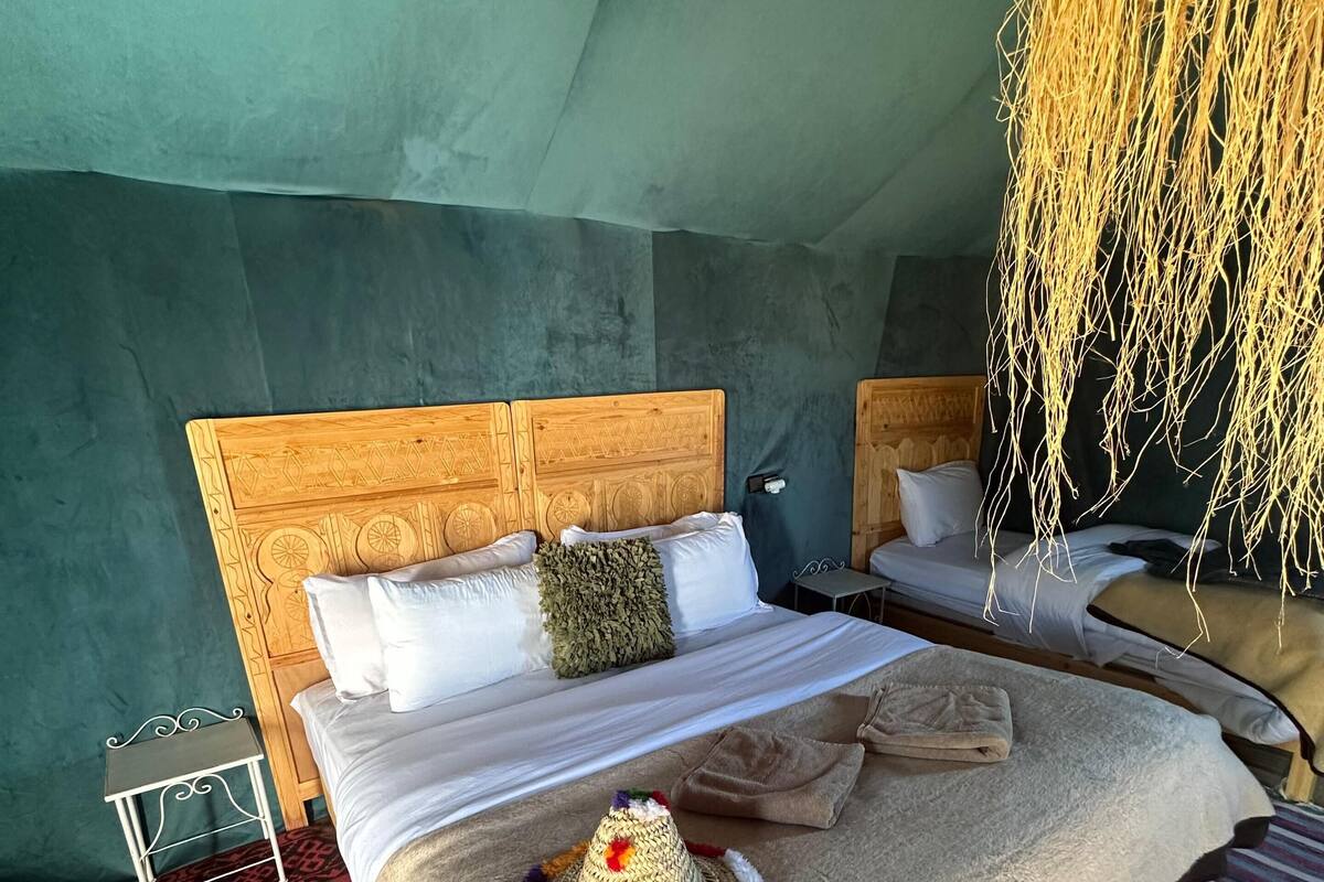 A room with a large bed, a small bedside table, and a hanging light fixture.