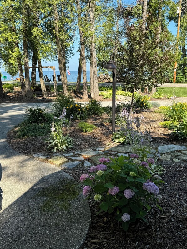 Un jardín con un sendero de piedra, plantas en flor y un conjunto de columpios con vista a un cuerpo de agua.