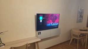 Ett rum med en väggmonterad tv som visar serien ”Stranger Things” på Netflix, ett skrivbord i trä, en stol och ett litet bord med en tallrik på.