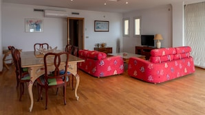 A dining area with a wooden table and chairs, a red sofa, and a television in the background. - Seafront apartment in Roses (Roses)