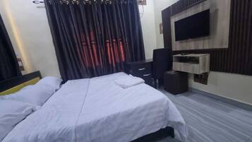 A hotel room with a bed, a desk, a chair, a TV, and an air conditioning unit.