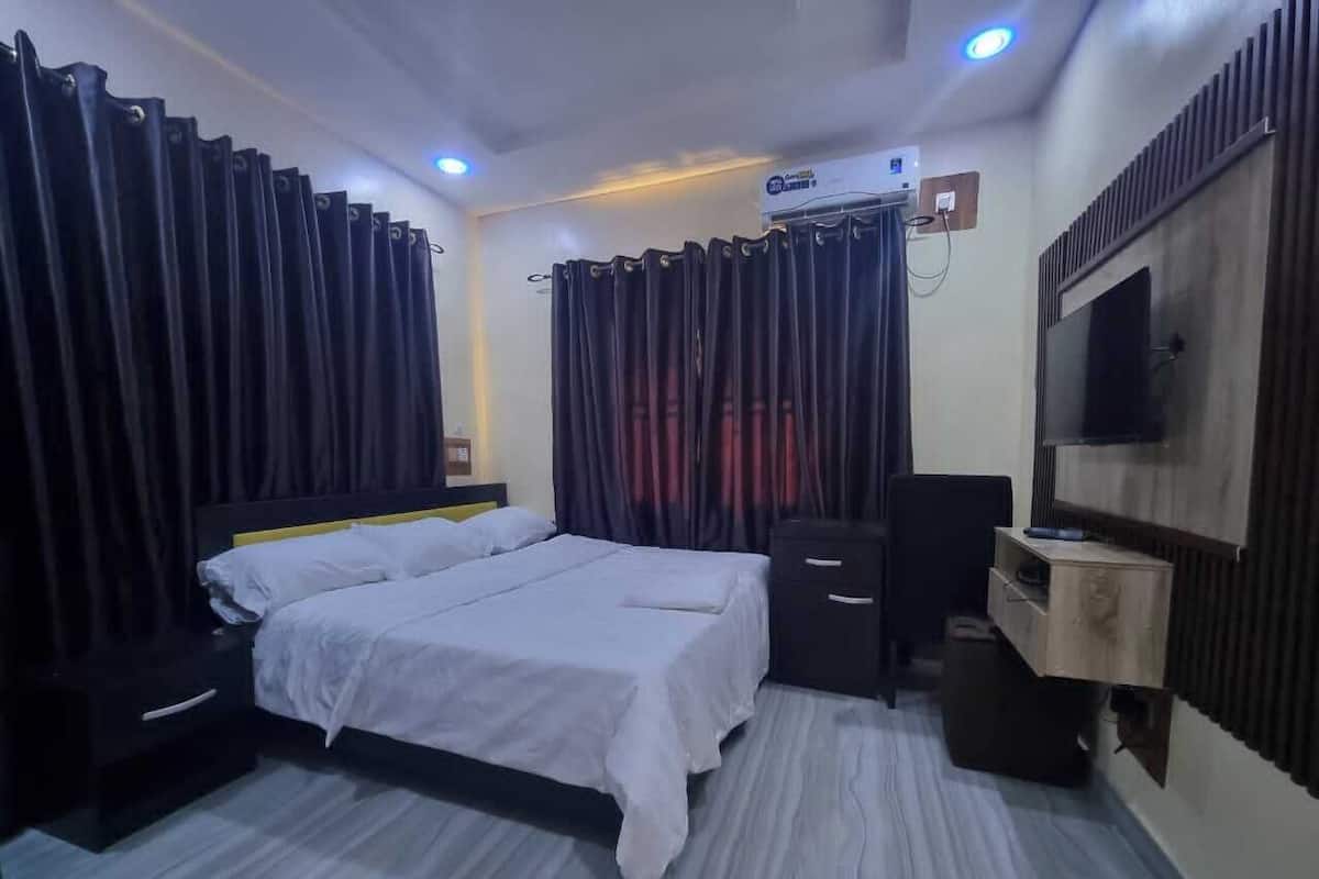 Quarto com duas camas, cômoda, televisão e estante embutida.