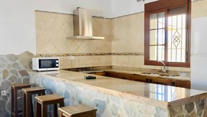 Cozinha com ilha de pedra, micro-ondas, fogão e janela com grades decorativas.