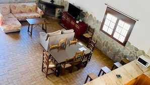 Uma sala de estar acolhedora com lareira de pedra, um sofá, uma mesa de jantar com cadeiras e uma cozinha com micro-ondas.