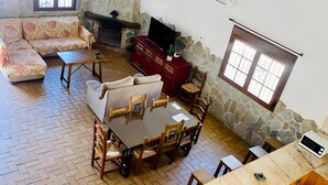 Uma sala de estar aconchegante com lareira de pedra, um sofá, uma mesa de jantar com cadeiras e uma cozinha com micro-ondas.