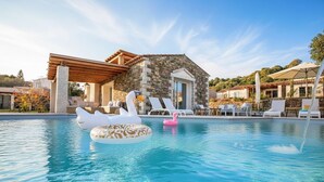 A pool with swan and flamingo floats, a stone building with a wooden pergola, and lounge chairs. - Villa del Borgo-Private pool, exclusive park, authenticity and luxury by the sea (Sardegna)