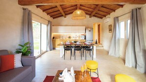 A spacious living area with a high wooden ceiling, a dining table set for four, and a kitchen in the background. - Villa del Borgo-Private pool, exclusive park, authenticity and luxury by the sea (Sardegna)