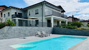 Una casa moderna de dos pisos con piscina, muros de piedra y un balcón con mobiliario exterior.
