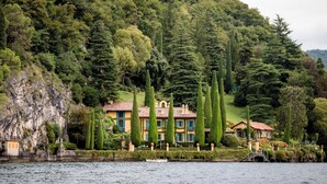 Una propiedad junto al lago con una casa grande rodeada de árboles altos y un risco rocoso.
