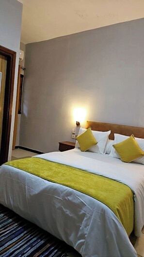A hotel room with a bed, nightstand, and wall-mounted lamp.