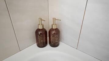 Baño con dos botellas marrones etiquetadas 'SHAMPOO' y 'SOAP' sobre una pared de azulejos blancos.