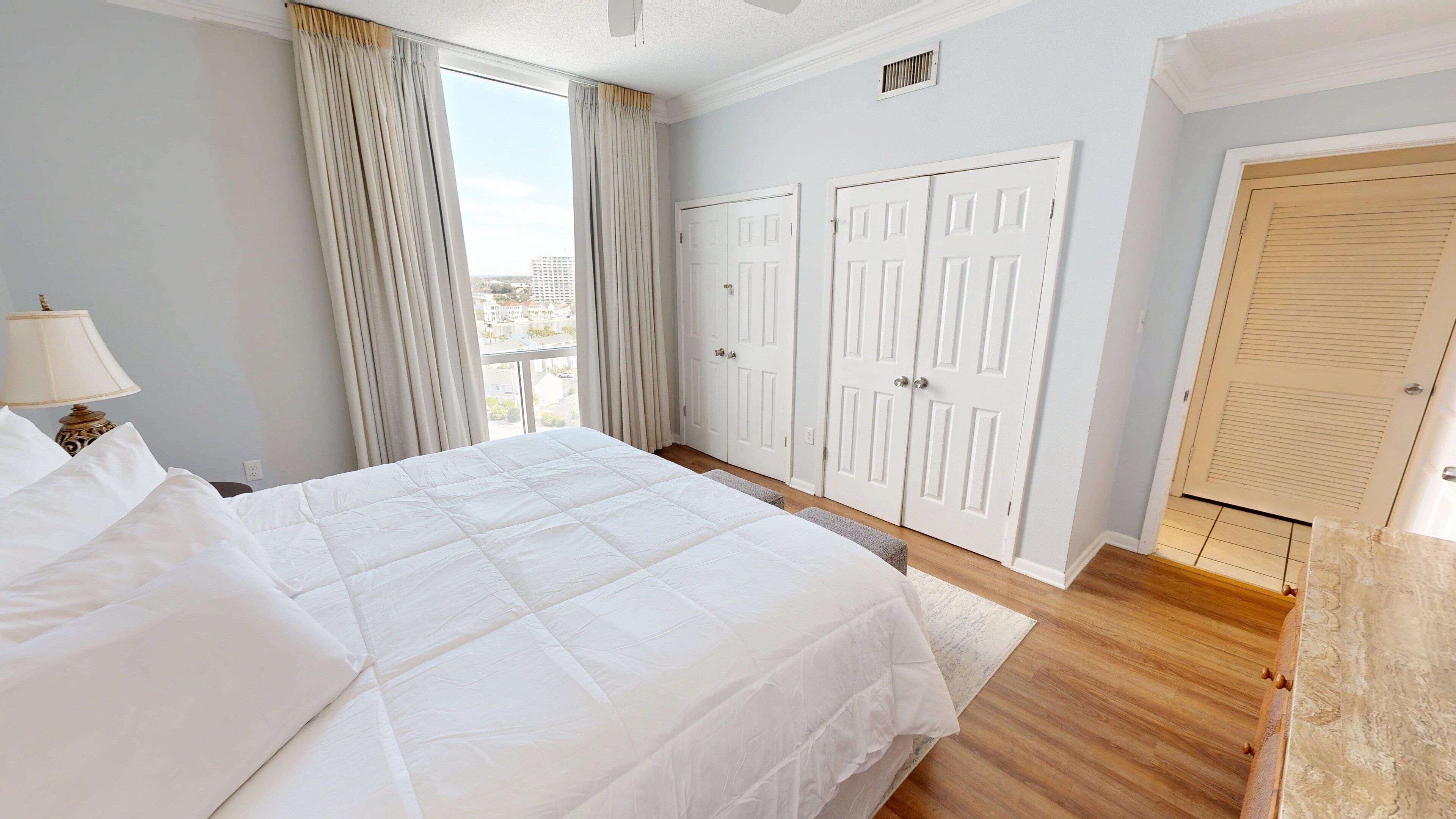 Camera d'albergo con un letto grande, un comodino, una lampada, una finestra con tende e un insieme di porte doppie.