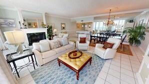 A spacious living room with a sofa, armchairs, a coffee table, and a dining area with a chandelier. - Shoreline Towers 2122 3 Bedroom Condo (Destin)