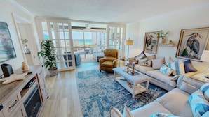 A spacious living room with a large window, a leather armchair, a sofa, and a coffee table. - Shoreline Towers 3054 2 Bedroom Condo (Destin)