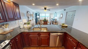 A modern kitchen with dark wood cabinets, stainless steel appliances, and a granite countertop. - Shoreline Towers 1033 2 Bedroom Condo (Destin)