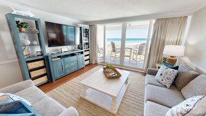 A living room with a TV, sofa, and a view of the beach. - Shoreline Towers 1033 2 Bedroom Condo (Destin)