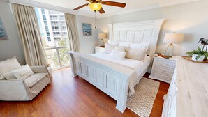 A bedroom with a large bed, a chair, a nightstand, a lamp, and a ceiling fan. - Shoreline Towers 1033 2 Bedroom Condo (Destin)