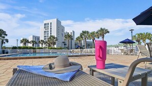 Zona de piscina con una silla de descanso, un sombrero de sol y una botella de agua rosa.