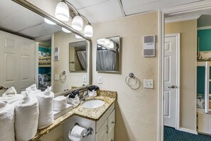 A bathroom with a sink, mirror, towel dispenser, and a shower curtain. - Casa Del Mar 309 1 Bedroom Condo (Galveston)