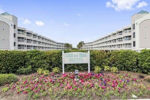 A sign for 'Casa del Mar Beachfront Rental Suites' with a symmetrical building layout and a landscaped flower bed in front. - Casa Del Mar 309 1 Bedroom Condo (Galveston)
