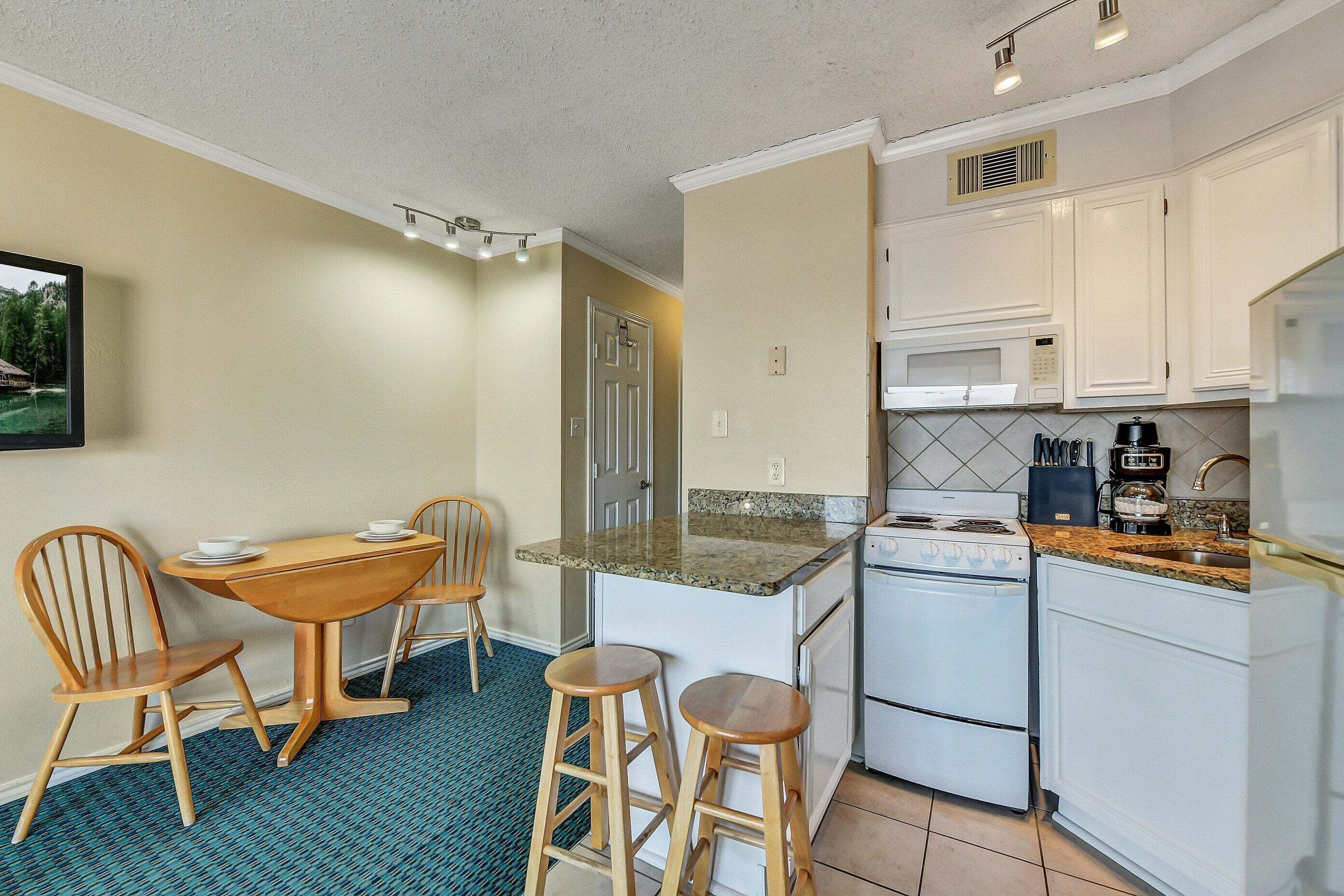 A compact kitchen with a dining area, featuring a small island, white cabinets, and a microwave.