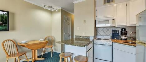 A compact kitchen with a dining area, featuring a small island, white cabinets, and a microwave.