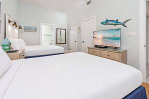 A hotel room with a large bed, a television, a desk with a lamp, and a door leading to another room. - Phoenix V 115 2 Bedroom Condo (Orange Beach)