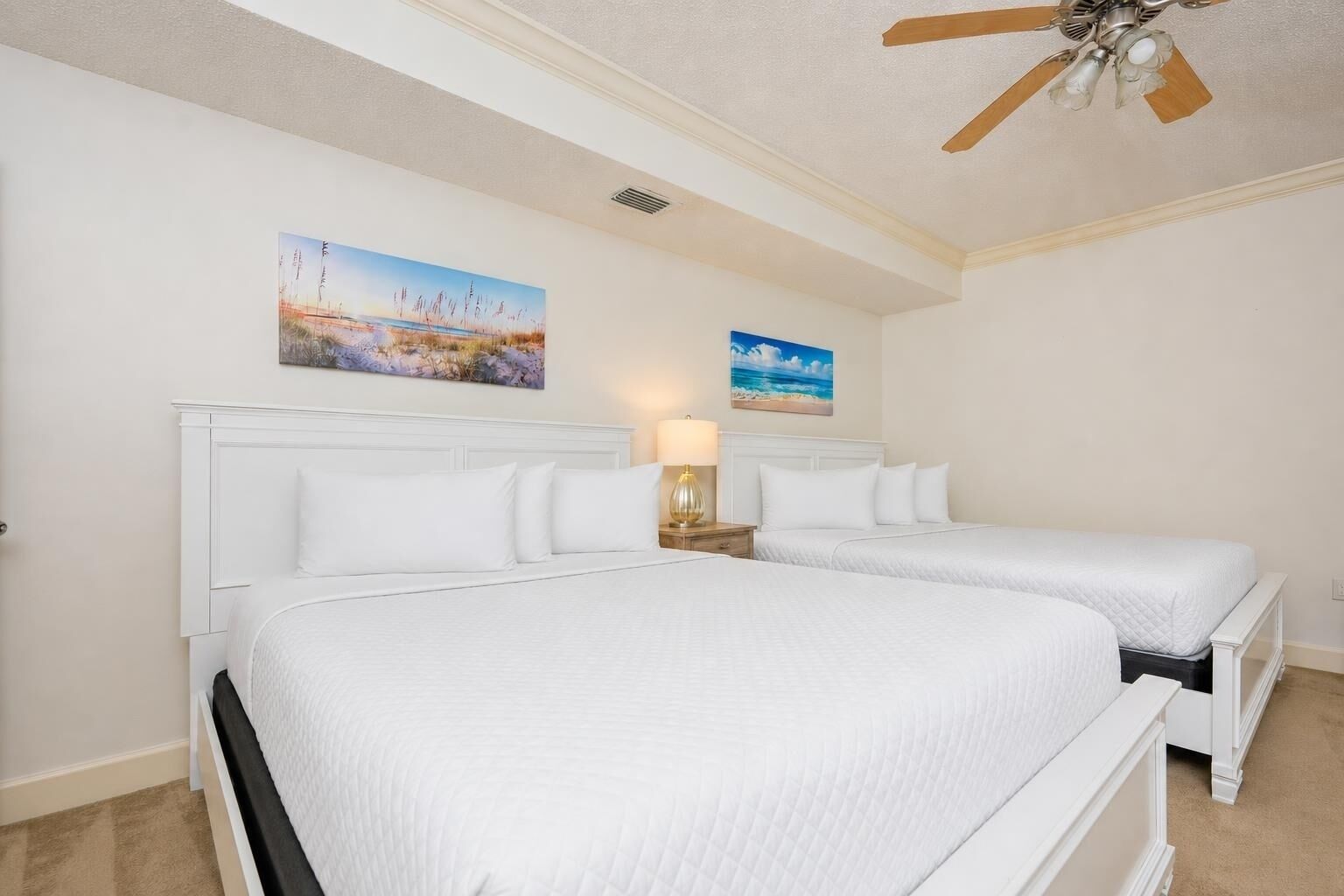 A hotel room with two beds, a ceiling fan, and two paintings on the wall.