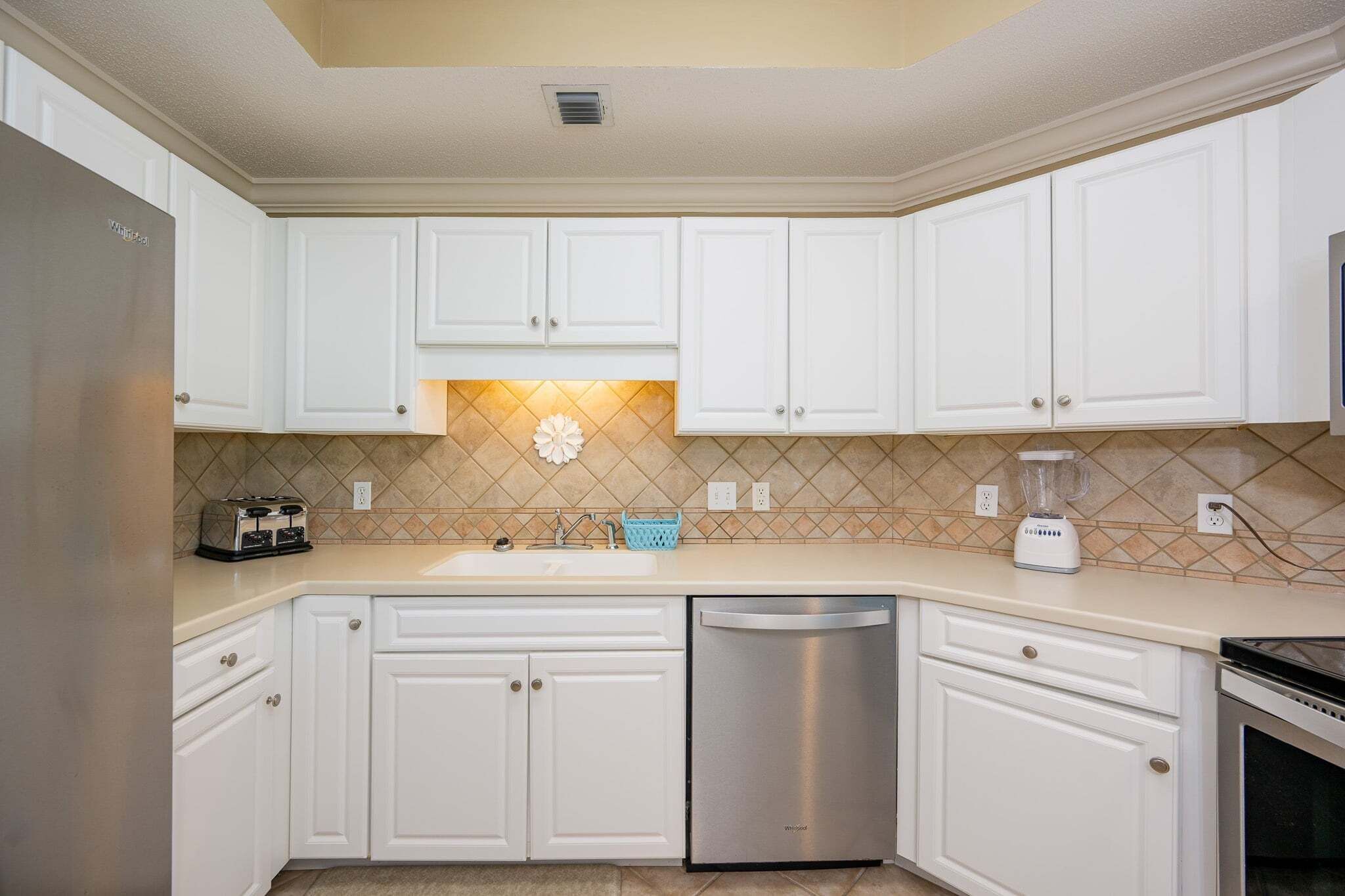 A kitchen with white cabinets, a stainless steel dishwasher, a toaster, and a blender on the countertop.
