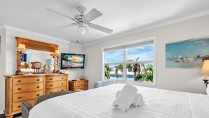 Une chambre d’hôtel avec un lit, un ventilateur de plafond, une télévision, une commode, une fenêtre donnant sur un beau paysage et un tableau accroché au mur.