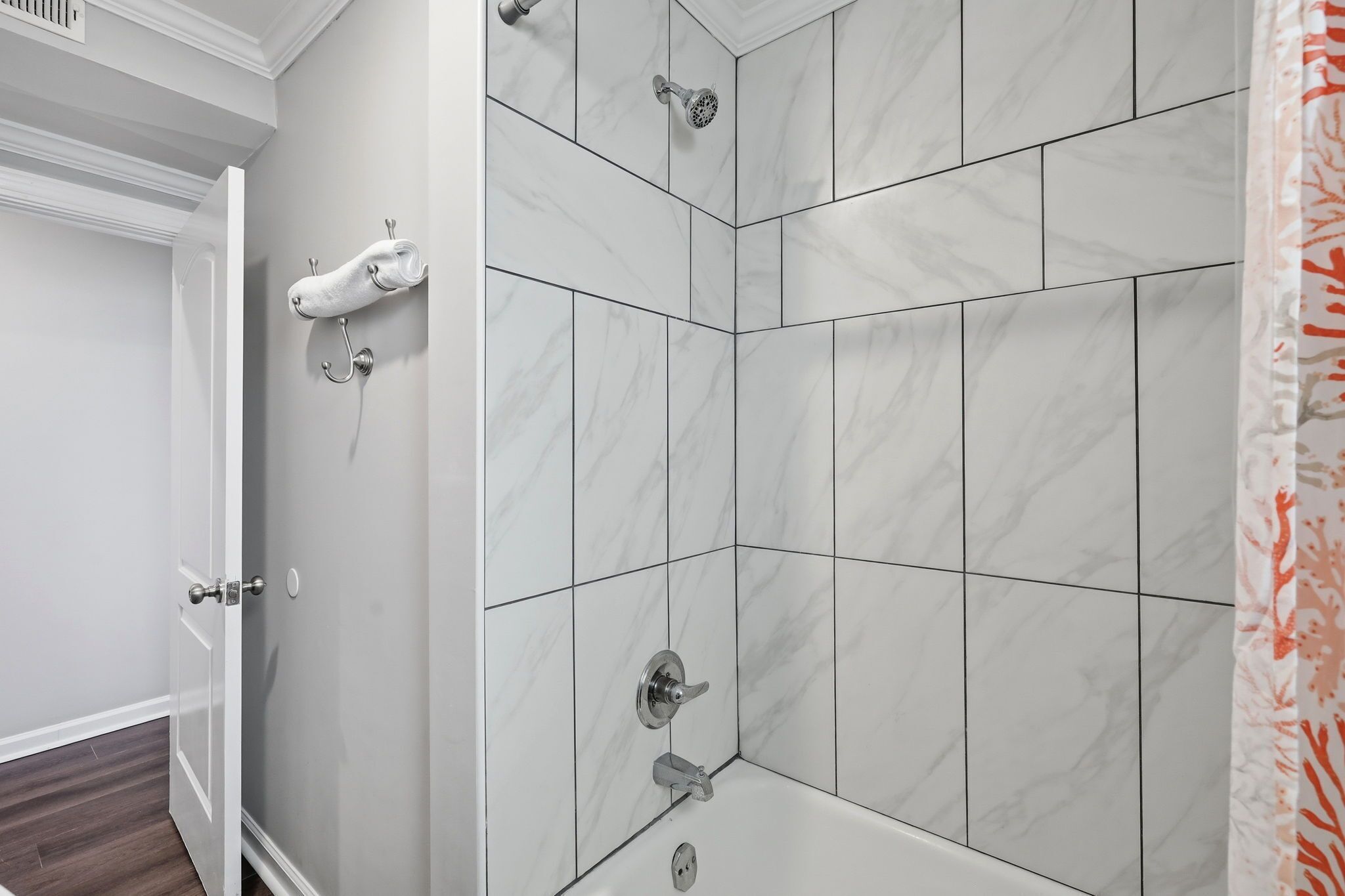 A bathroom with white marble tiles, a shower with a handheld showerhead, and a towel rack.