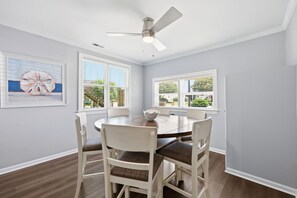 A dining area with a round table, white chairs, ceiling fan, and large windows with blinds. - Bayview Anchor-Pet Friendly Home with Dock (Atlantic Beach)
