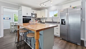 Eine moderne Küche mit weißen Schränken, einer Holztischinsel mit Barhocker, Edelstahlgeräten und einem großen Kühlschrank.