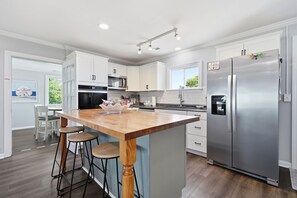 A modern kitchen with white cabinets, a wooden island with stools, stainless steel appliances, and a large refrigerator. - Bayview Anchor-Pet Friendly Home with Dock (Atlantic Beach)