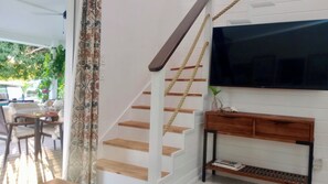 A staircase with wooden steps and rope handrails, a flat-screen TV mounted on the wall, and a wooden console table with a plant and books.