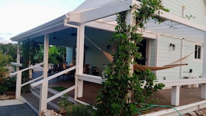 A covered outdoor area with a wooden deck, a hammock, and a dining table with chairs.