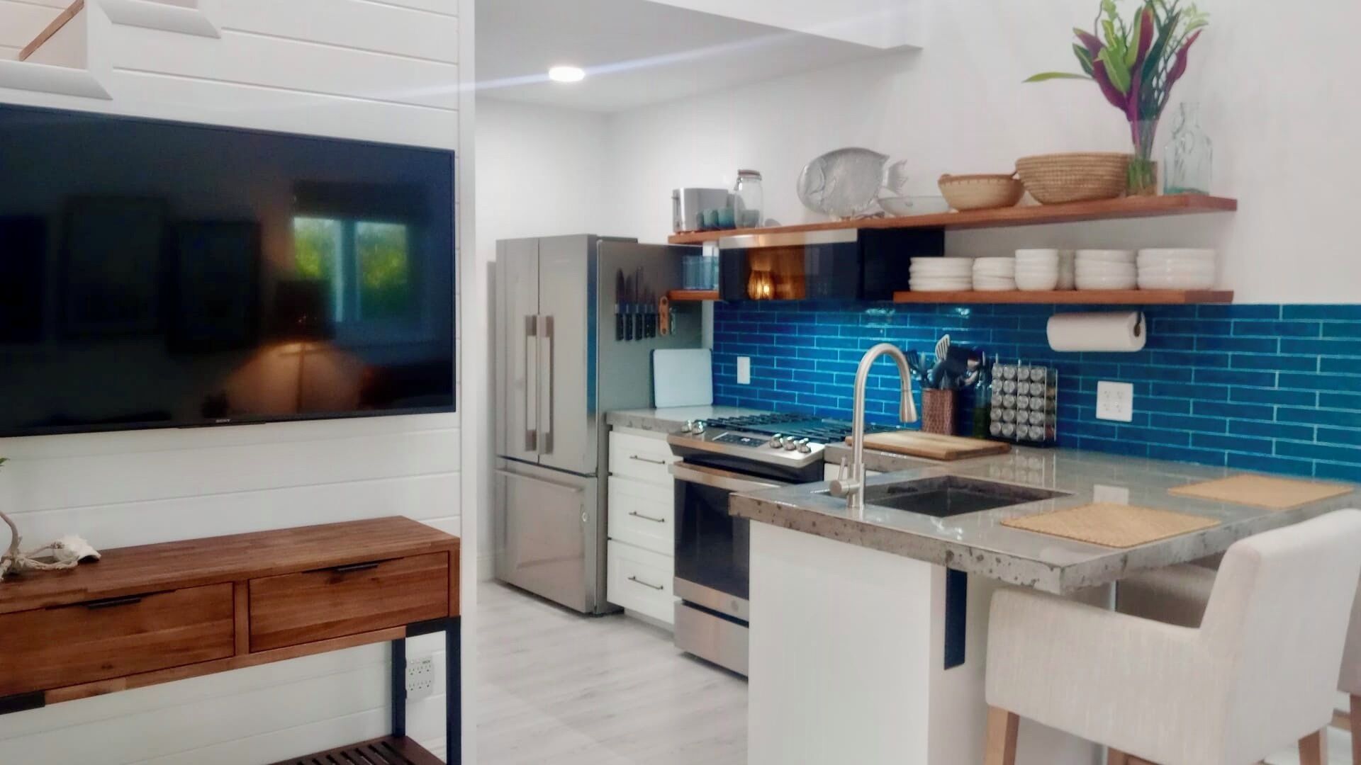 A modern kitchen with a built-in oven, stainless steel appliances, a blue backsplash, and a wooden dining table.