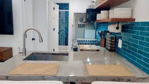 A kitchen with a stainless steel sink, a stove, and a blue tiled backsplash.