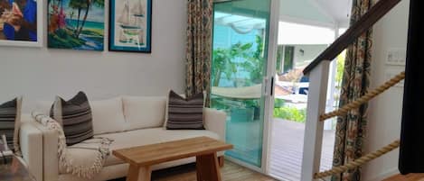 A living room with a white sofa, a wooden coffee table, and a glass door leading to a balcony with a hammock.