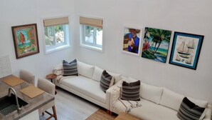 A modern living room with a white sofa, a dining table with chairs, and artwork on the walls.