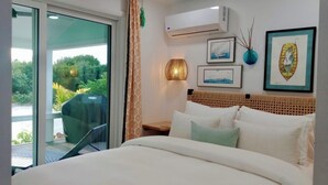 A hotel room with a bed, a chair, a table, and a view of greenery outside.