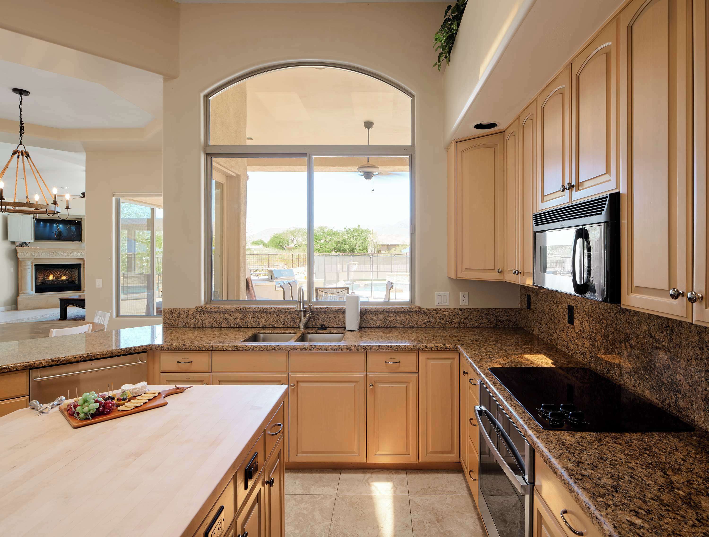 A kitchen with granite countertops, wooden cabinets, a built-in oven, and a large window overlooking a patio.