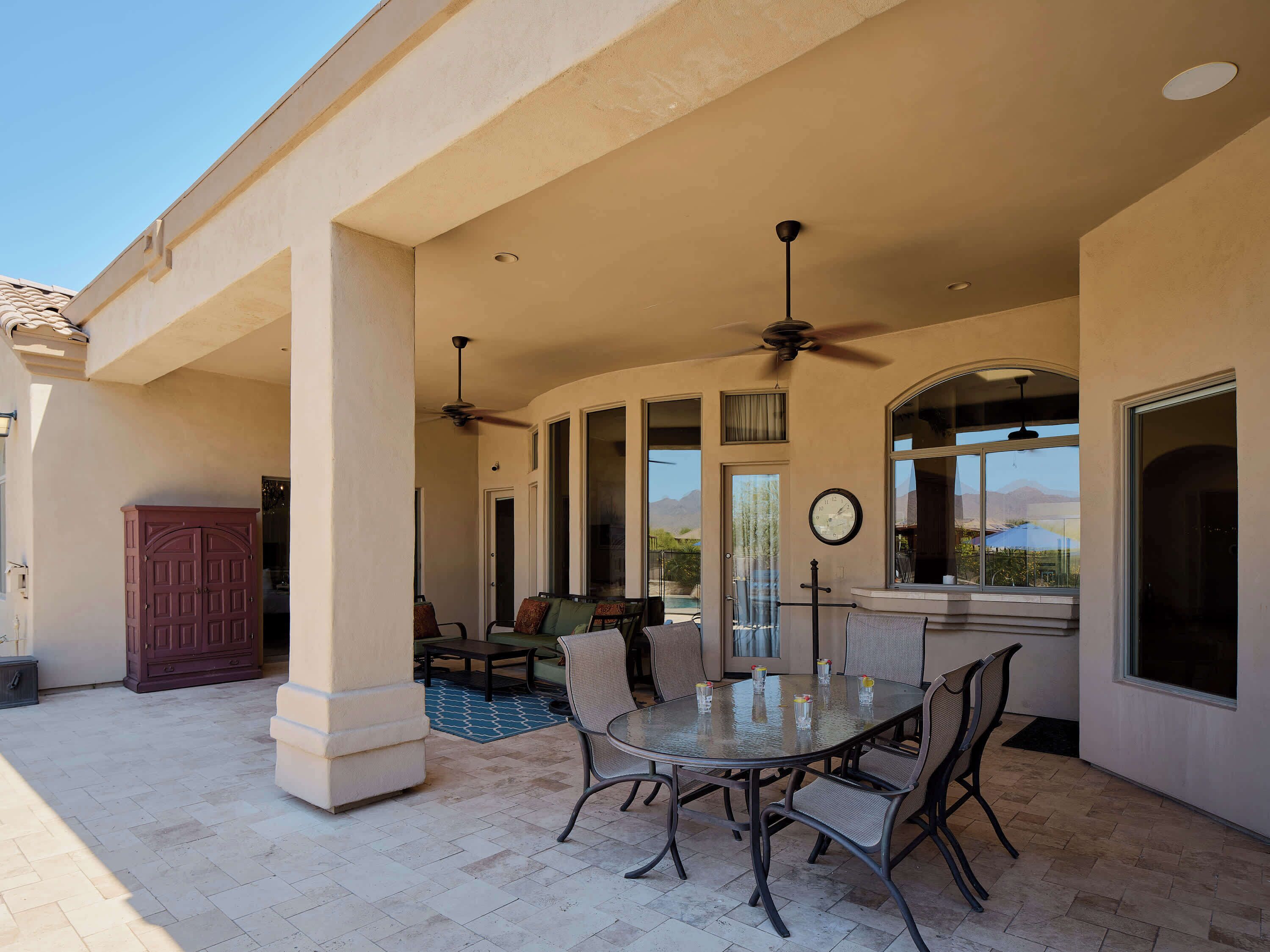 A covered patio with a glass table and chairs, a ceiling fan, and a view of mountains.