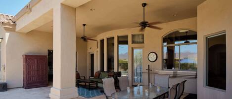 A covered patio with a glass table and chairs, a ceiling fan, and a view of mountains.