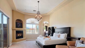 A bedroom with a large bed, a fireplace, a chandelier, a bookshelf, and a view through a window. - The Family Room-Pool & Outdoor Games-Game Room (Scottsdale)