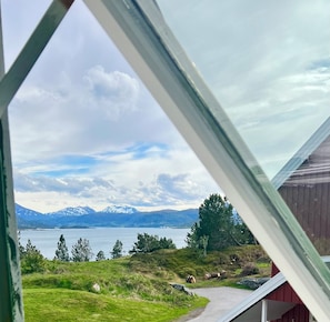 A view through a window of a mountainous landscape with a lake, trees, and a red building. - Vintage apartment with pets (Møre og Romsdal)