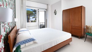 Ein Schlafzimmer mit Bett, Schrank, Fenster und Blick auf Bäume.