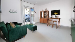 Ein Wohnzimmer mit einem grünen Sofa, einem Holzschrank und einem Essbereich mit Hockern.